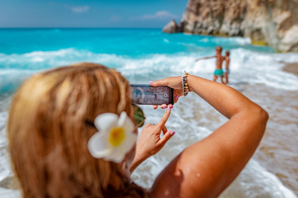 Женщина снимает детей на камеру смартфона на пляже в Греции